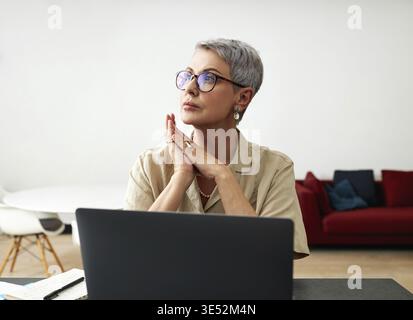 Stilvolle reife Frau in Brille am Schreibtisch sitzen Stockfoto