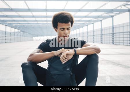 Junge Mann sitzt im Freien mit einem Fitness Tracker seine Fortschritte zu überwachen Stockfoto