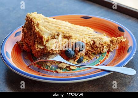 Ein köstliches Stück Kuchen mit Blaubeeren auf einem farbenfrohen Teller, bereit zum Genießen. Eine silberne Gabel wird für ein süßes Dessert platziert Stockfoto