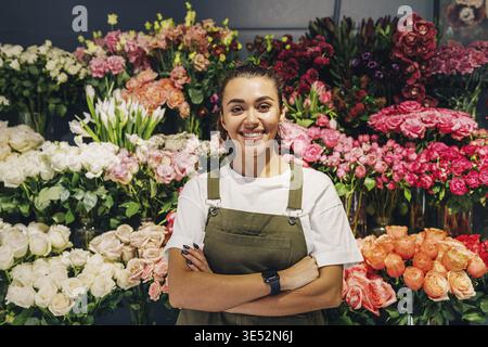 Blumenfrau steht im Blumenladen. Floristin in Schürze stehend mit überkreuzten Armen Stockfoto