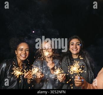Drei glückliche Weibchen mit Wunderkerzen. Eine Gruppe verschiedener weiblicher Freunde am Abend Stockfoto