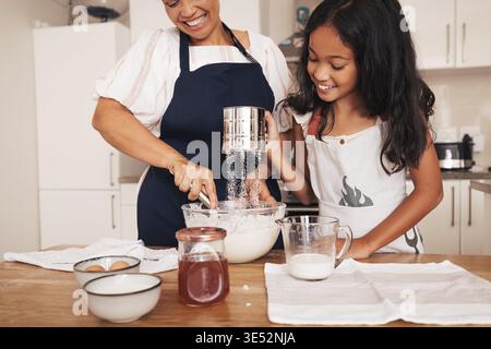 Seniorin und Enkelin sieben Mehl an einem Tisch in der Küche. Mädchen und ihre Oma machen Teig Stockfoto
