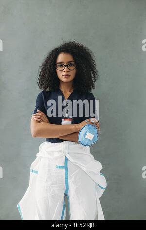 Junge Brillenspezialistin mit Maske, Schutzanzug und Uniform Stockfoto