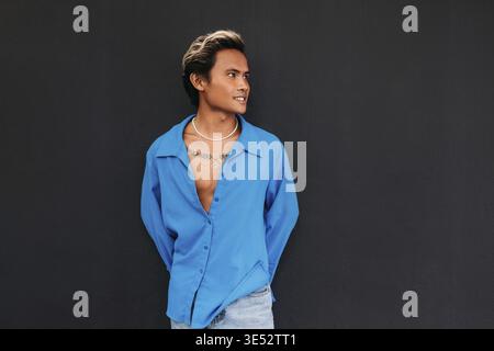 Junger, stylischer Typ in blauem Hemd, der an der schwarzen Wand posiert Stockfoto
