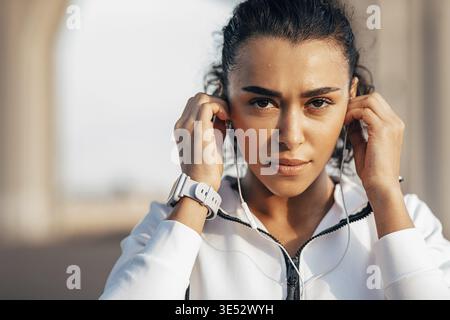 Nahaufnahme Porträt einer schweißtreibendem Sportlerin, die ihre Kopfhörer während eines Trainings justiert Stockfoto