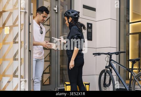 Frau, die als Kurier arbeitet. Die Lieferfrau scannt Barcode, während der Kunde eine Kiste hält Stockfoto