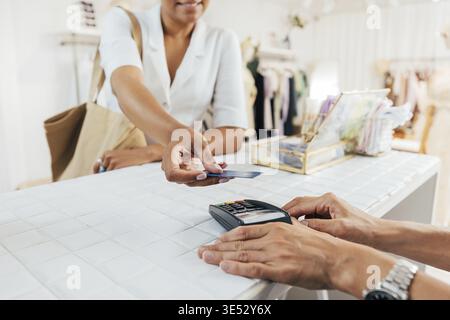 Eine kurze Aufnahme der Hände einer Verkäuferin, die das POS-Terminal hält, während eine Kundin per Kreditkarte zahlt Stockfoto