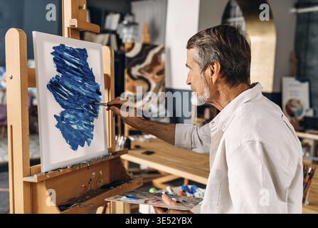 Begeisterter Künstler, der in seinem Studio auf Leinwand arbeitet Stockfoto