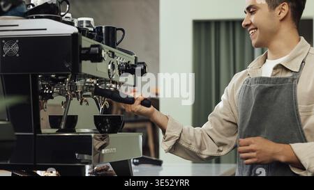 Zugeschnittene Aufnahme eines jungen Barista mit einer Kaffeemaschine. Lächelnder männlicher Barista, der die Kaffeemaschine anpasst Stockfoto