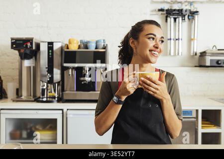 Weibliche Kellnerin hält Kaffeetasse, während sie am Tisch im Café steht Stockfoto