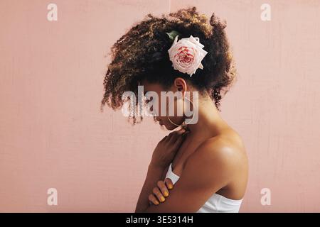 Seitenansicht einer jungen Frau mit rosa Blüten in ihrem lockigen Haar Stockfoto