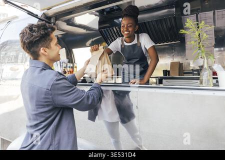 Seitenansicht eines jungen Mannes, der von einer Verkäuferin Pakete mit Straßenessen nahm Stockfoto