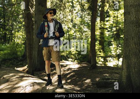 Selbstbewusster Senior Tourist, der mit Rucksack im Wald steht und wegblickt Stockfoto