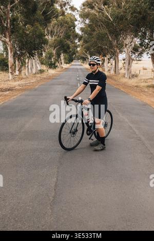 Junge Frau in Sportkleidung, die mit dem Fahrrad auf einer leeren Straße steht Stockfoto