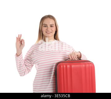 Glückliche junge Frau mit Koffer, die eine gute Geste auf weißem Hintergrund zeigt Stockfoto