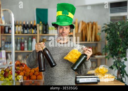 Erwachsener positiver männlicher Käufer in grünem Kostüm und Hut, Einkaufsflaschen mit festlichem Bier für St. Patrick's Day Stockfoto