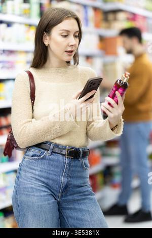 Junge Frau scannt QR-Code auf Pflegeprodukten Stockfoto