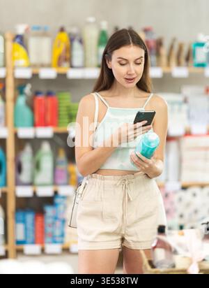 Frau, die Haarshampoo auf ihrem Handy im Supermarkt scannt Stockfoto