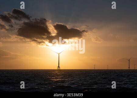 Offshore-Windturbinen, die sich vor einem strahlenden Bernsteinuntergang über der Nordsee abschirmen und hinter der Windenergieanlage durch die Wolken brechen. Stockfoto