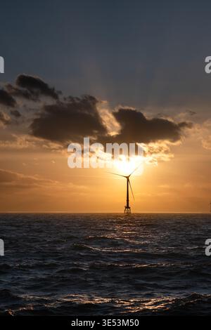 Offshore-Windturbinen, die sich vor einem strahlenden Bernsteinuntergang über der Nordsee abschirmen und hinter der Windenergieanlage durch die Wolken brechen. Stockfoto
