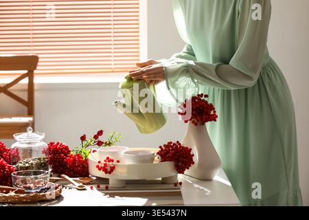 Junge Frau, die zu Hause Viburnum-Tee aus der Teekanne in eine Tasse gießt Stockfoto