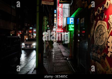 Regnerische Nacht in Tenmonkan, Kagoshima. Fängt Reflexionen in leuchtenden Neontönen auf nassen Strecken und ruhigen Straßen ein und zeigt einen authentischen städtischen geldautomaten Stockfoto