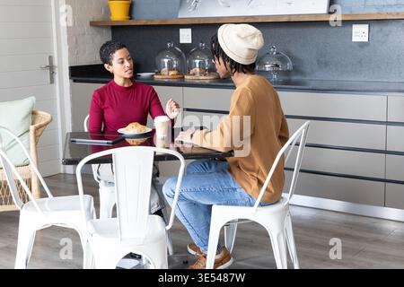 Afroamerikanische Freunde unterhalten sich am Glastisch mit Croissant und Telefon im Café Stockfoto
