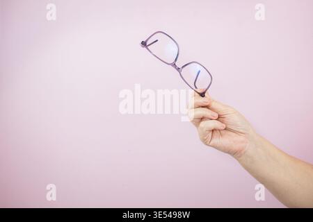 Nahaufnahme einer Hand mit einer stilvollen Brille im Optikergeschäft zur Korrektur und zum Kauf des Sehvermögens. Frau Hand hält Brille auf hellem Hintergrund Witz Stockfoto