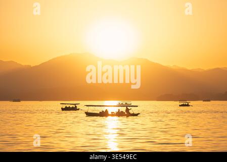 Goldener Sonnenuntergang über dem Westsee mit traditionellen Booten für Passagiere in Hangzhou, China Stockfoto