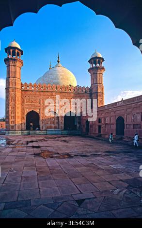 Die Badshahi-Moschee in Lahore zeigt historische Elemente unter hellem Himmel. Besucher spazieren im Innenhof, während die Sonne auf Details der Struktur scheint. Stockfoto