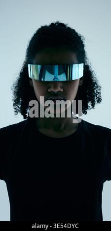 Nahaufnahme-Porträt einer weiblichen Teenager-Athletin mit verspiegeltem futuristischem Visier bei minimaler Studiobeleuchtung. Stockfoto
