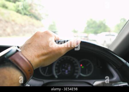 Auto fährt auf der Straße, Nahaufnahme der Hand eines Fahrers auf einem Lederlenkrad, trägt eine braune Lederuhr, mit dem Armaturenbrett im Stockfoto