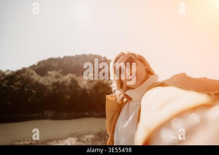 Woman Sunglasses Mountain - Porträt einer Frau, die eine Sonnenbrille trägt und draußen lächelt, mit einem Berg im Hintergrund. Stockfoto
