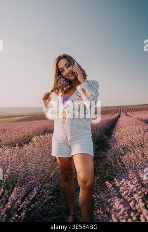 Frau Lavendel Smartphone steht im blühenden violetten Feld, während sie bei Sonnenuntergang auf dem Handy spricht Stockfoto