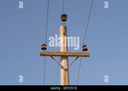 Verwitterter Holzmast mit elektrischen Leitungen, klarem blauem Himmel, Keramikisolatoren und rostfreien Armaturen, vertikale Komposition zur Hervorhebung der Textur und Einfachheit Stockfoto