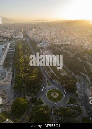 Aus der Vogelperspektive auf den üppigen Stadtpark, die historische Alcazaba und einen zentralen Kreisverkehr bei einem goldenen Sonnenuntergang in Malaga, Andalusien, Spanien. Stockfoto