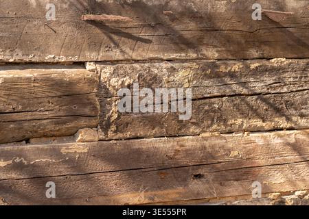Sonnendurchflutete, verwitterte Holzdielen mit tiefen Spalten und schattigen Rillen. Horizontale Nahaufnahme von wiederaufbereiteten Brettern mit Patina, knotigen Kanten und Oberfläche Stockfoto