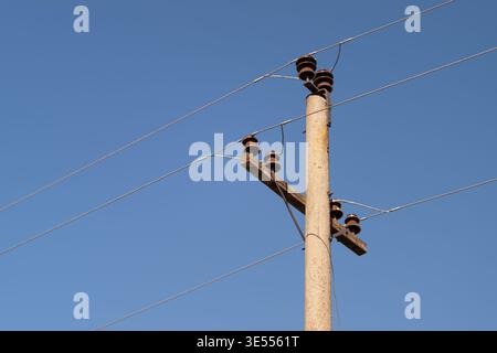 Verwitterter Holzmast mit elektrischen Leitungen, klarem blauem Himmel, Keramikisolatoren und rostfreien Armaturen, vertikale Komposition zur Hervorhebung der Textur und Einfachheit Stockfoto