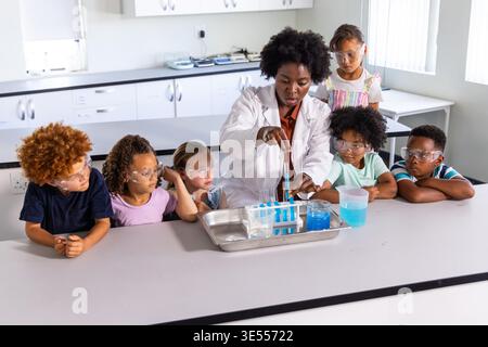 Afroamerikanischer Lehrer, der die chemische Demonstration auf dem Labortisch mit Kindern im weißen Mantel mit Pipette führt. Pädagoge, Studenten, Wissenschaft, Klassenzimmer, Labor, Experiment, Sicherheit || Modell veröffentlicht Stockfoto