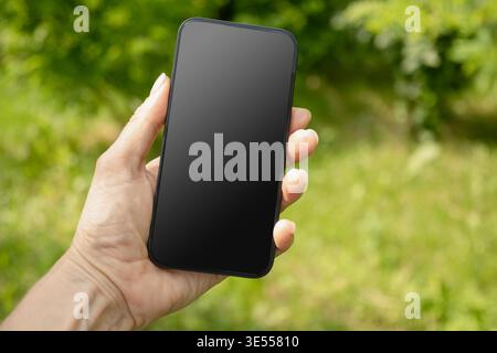 Nahaufnahme von Frauenhänden, die das Smartphone in grüner Umgebung halten. Überprüfen Sie Apps, die sich auf Geräte, Chats und Leistungsdaten konzentrieren. Sprachassistent. Fitnessfortschritt auf App. Platz für Design auf dem Bildschirm. Stockfoto