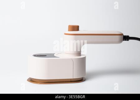 Modernes, kompaktes Dampfbügeleisen in weiß mit braunen Akzenten auf dem integrierten Standfuß. Seitlich vor sauberem weißem Hintergrund aufgenommen Stockfoto