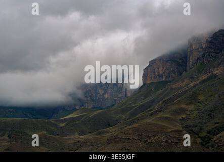 Majestätische Bergklippen, die an einem bewölkten Tag in dichten Wolken über grünen Hügeln gehüllt sind Stockfoto