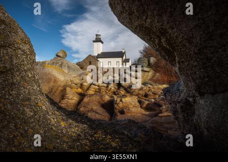 Blick auf den Leuchtturm von Phare de Pontusval, eingerahmt von massiven Granitblöcken unter einem blauen Himmel mit schimmernden Wolken in Plouneour-Brignogan-plages, Bretagne, F Stockfoto
