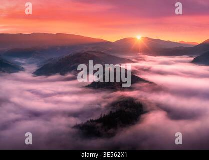 Luftaufnahme von Bergen in niedrigen Wolken bei Sonnenaufgang im Herbst Stockfoto