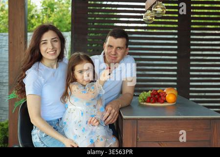 Glückliche Familie mit Kind, das draußen am Holztisch sitzt Stockfoto
