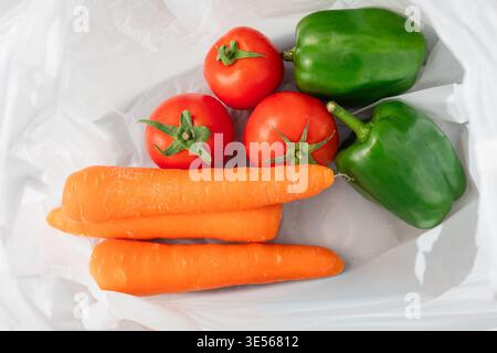 Gemischtes frisches Bio-Gemüse, einschließlich rote Tomaten, grüne Paprika und Orangenmohröhren, auf weißen Tellern und Holzschneidebrettern, M Stockfoto