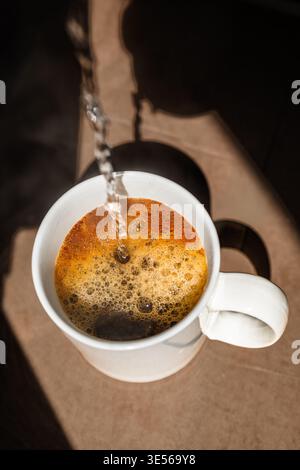Frisches heißes Wasser wird in eine weiße Keramikschale mit Instantkaffee mit goldenem Schaum gegossen. Stockfoto