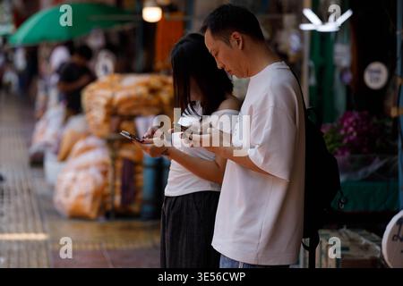 BANGKOK, THAILAND-22. März 2026: Touristen-Paar mit Telefonen auf dem Straßenmarkt, Reise-Lifestyle und digitales Verhalten, Seitenprofil, Pak Khlong Talat. Stockfoto