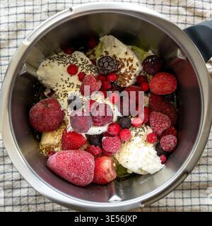 Draufsicht auf proteinreiche Smoothie-Zutaten, einschließlich Quark, Banane, gefrorene Beeren, Chiasamen und Leinsamen im Mixbecher. Gesunde Fitness Stockfoto
