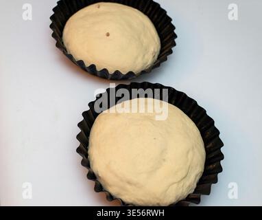 Roher Teig, der für traditionelles Osterbrot in Backformen auf hellem Hintergrund zubereitet wird. Hausgemachtes Backkonzept. Stockfoto